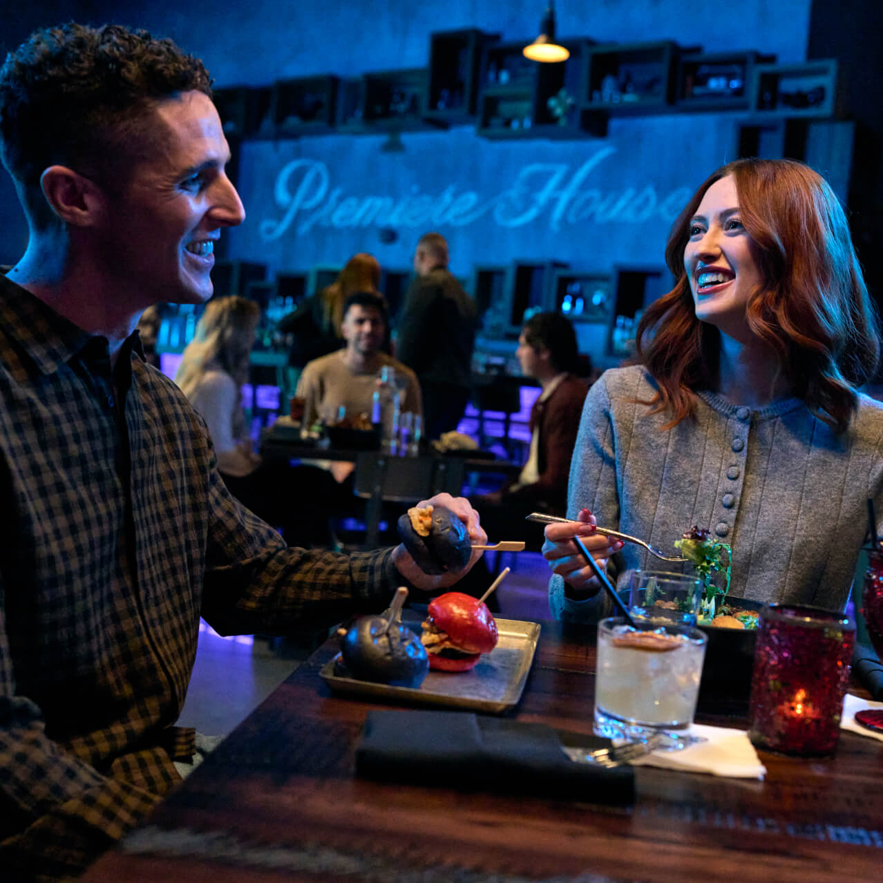 A man and woman laugh over food and drinks at Premiere House at Universal Horror Unleashed.