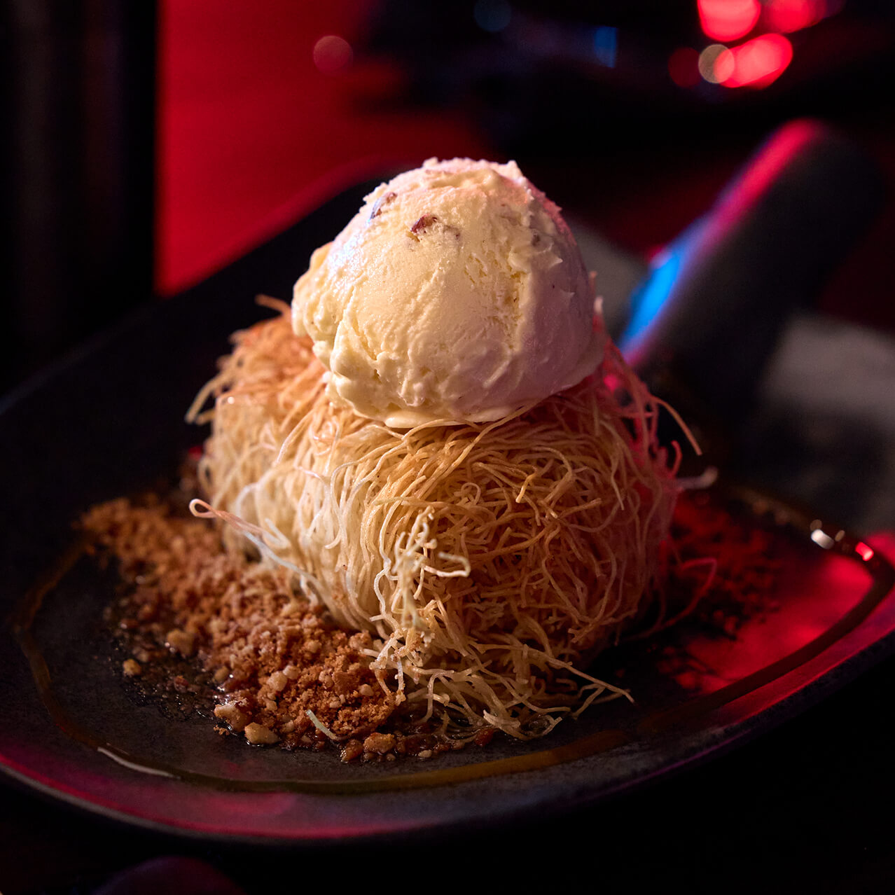 Shredded pastry dessert topped with a scoop of ice cream and crumbs on a plate.