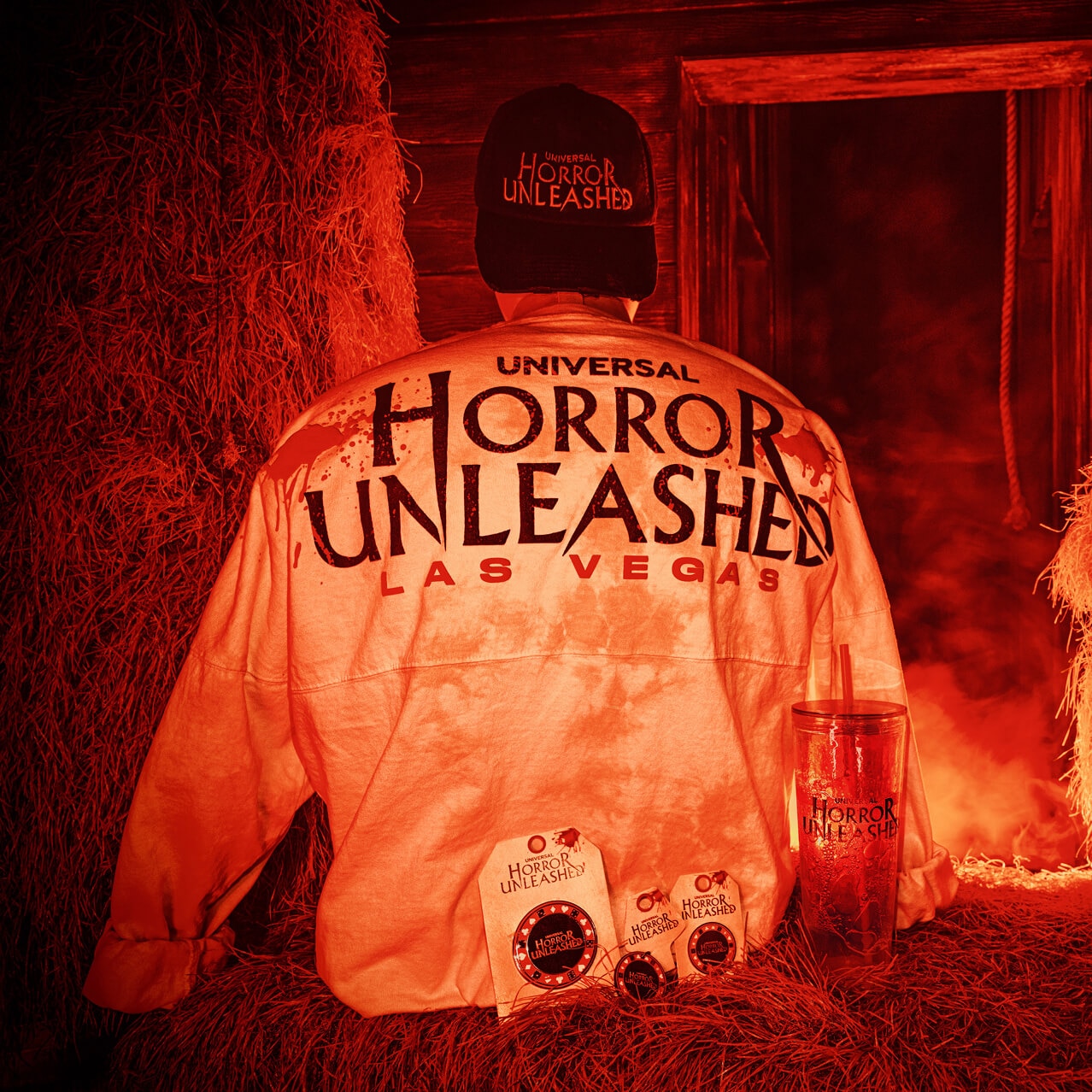 Universal Horror Unleashed Las Vegas merchandise including jersey, hat, pins, and tumbler displayed on hay.