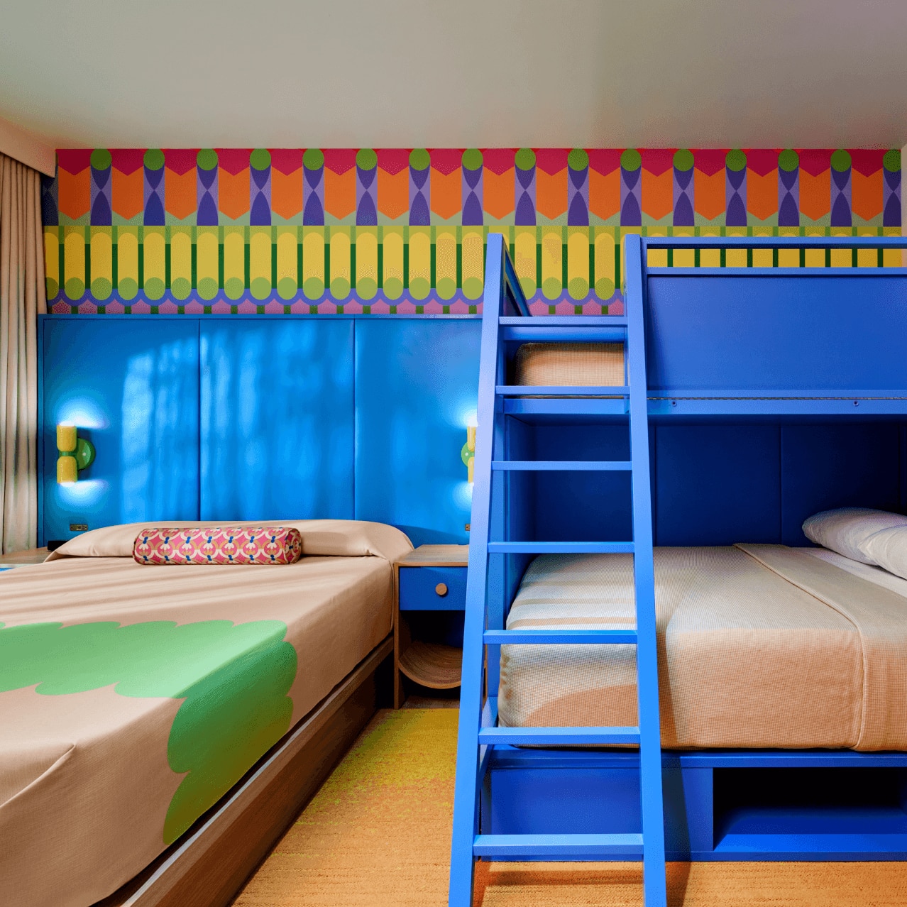 Standard room with blue bunk beds, a full bed and nightstands against a brightly colored accent wall.