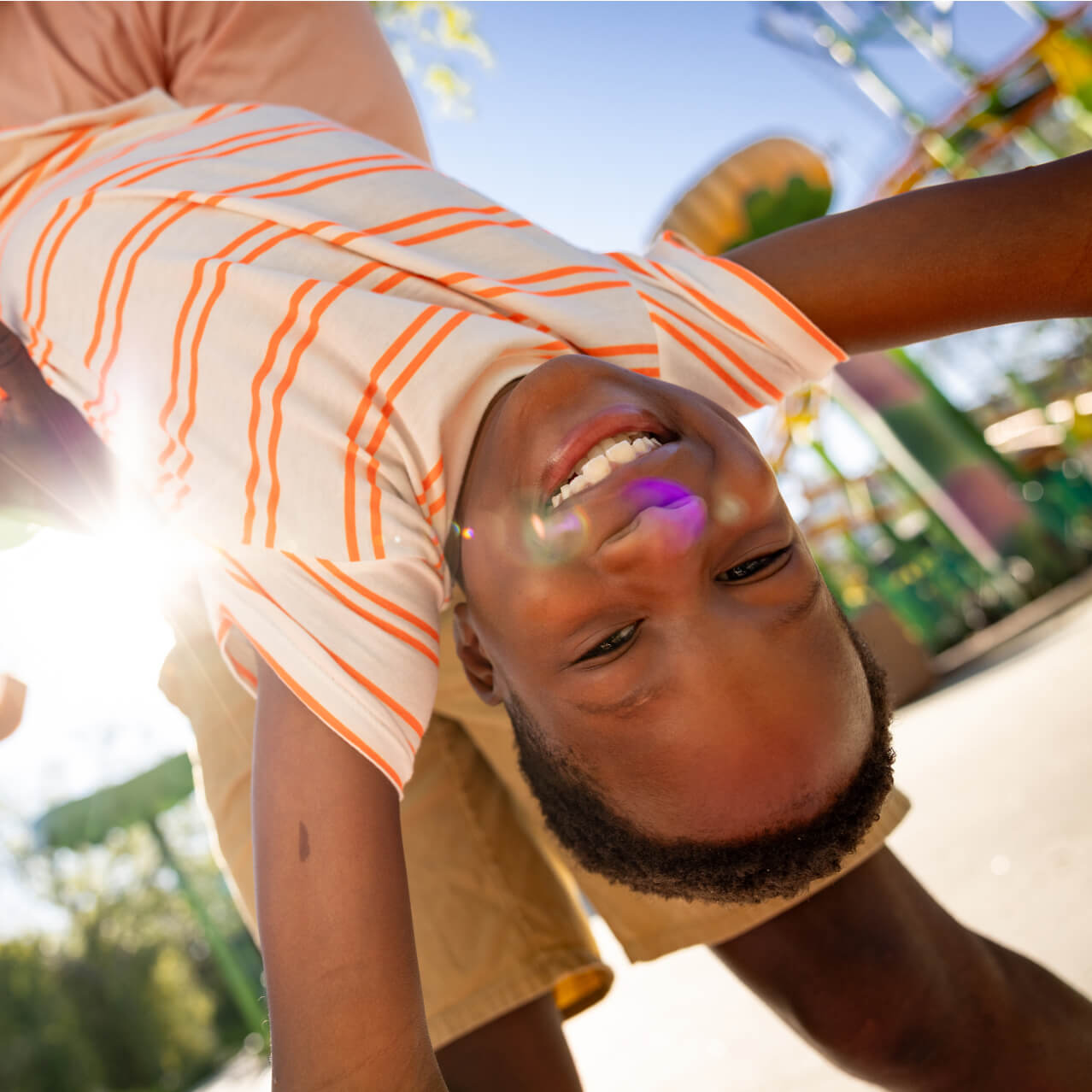 A child smiling while hanging upside down, with colorful theme park rides in the background.
