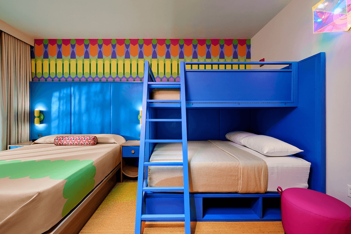 Standard room with blue bunk beds, a full bed and nightstands against a brightly colored accent wall.