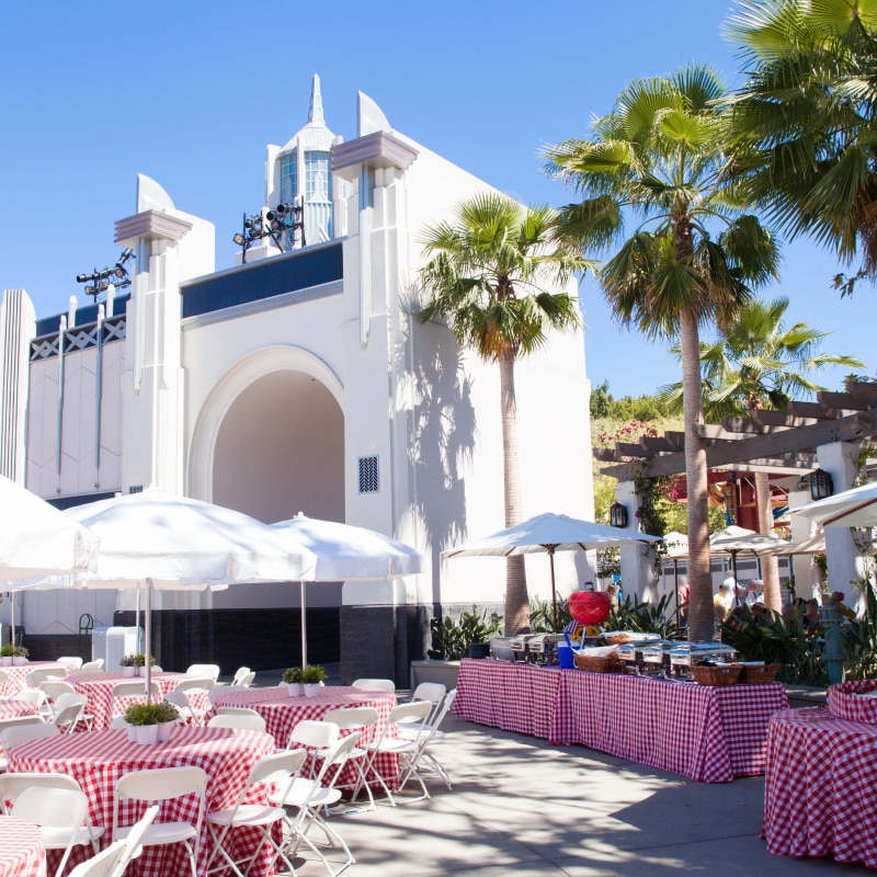 Tables with red checkered tablecloths and white umbrellas set up for an event inside of Universal Plaza.