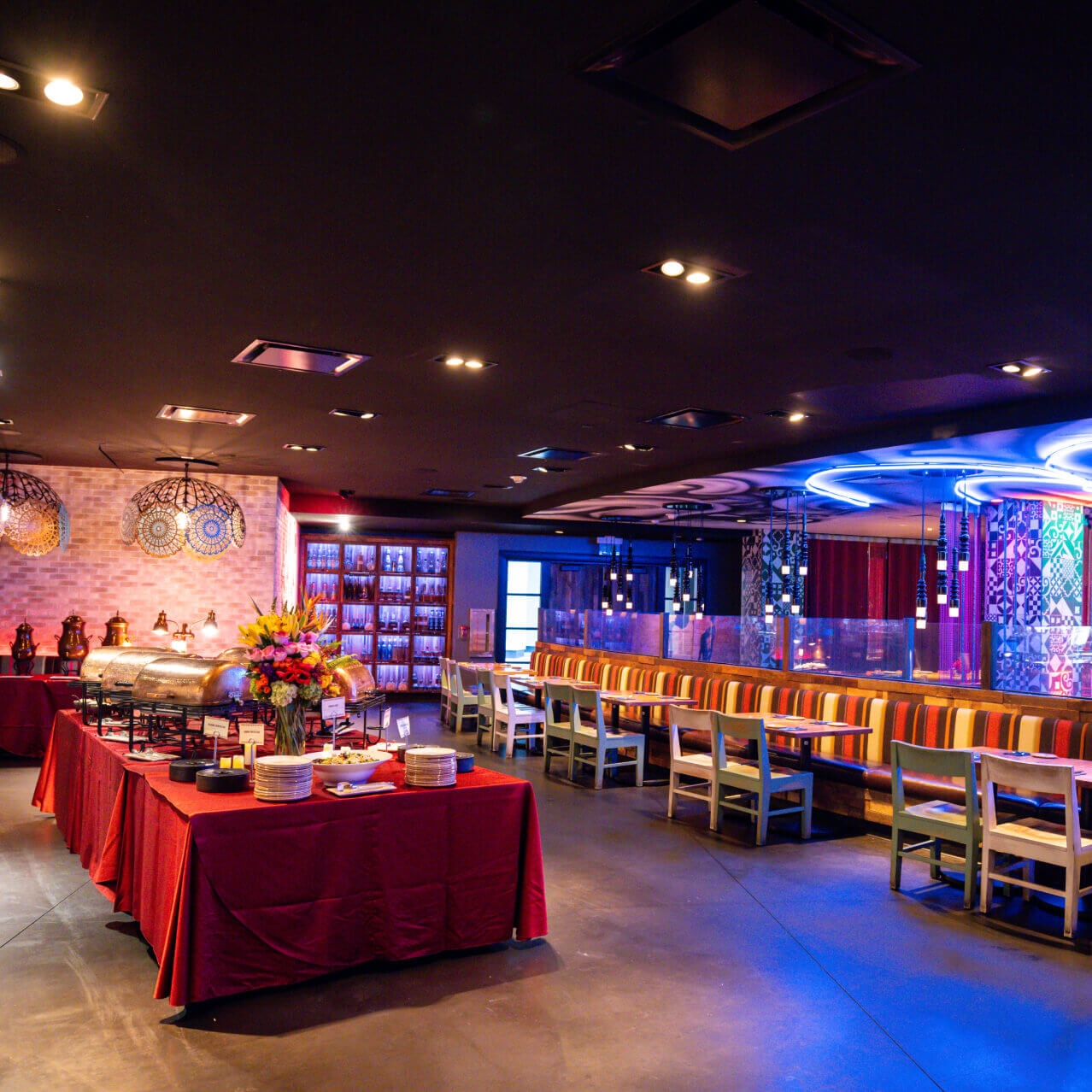 Various dishes and flowers set up on red tablecloth in a colorful restaurant interior with neon lights and booth seating.