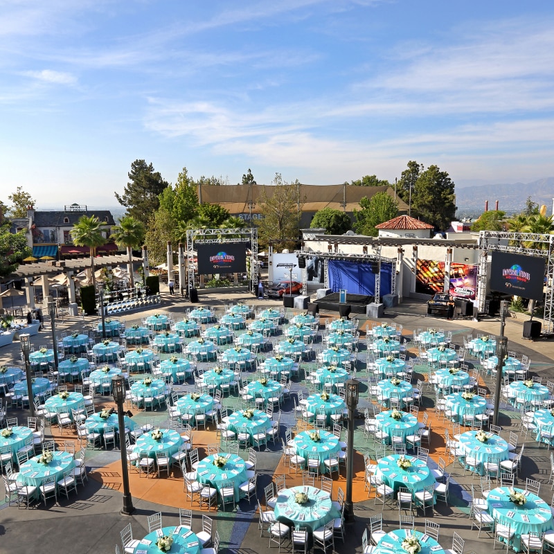 An aerial view of dozens of tables with teal tablecloths and floral centerpieces set up for an event inside of Universal Plaza.