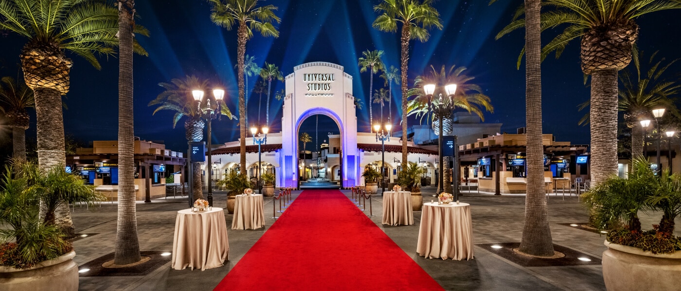 Universal Studios Hollywood front entrance with red carpet and palm trees at night.