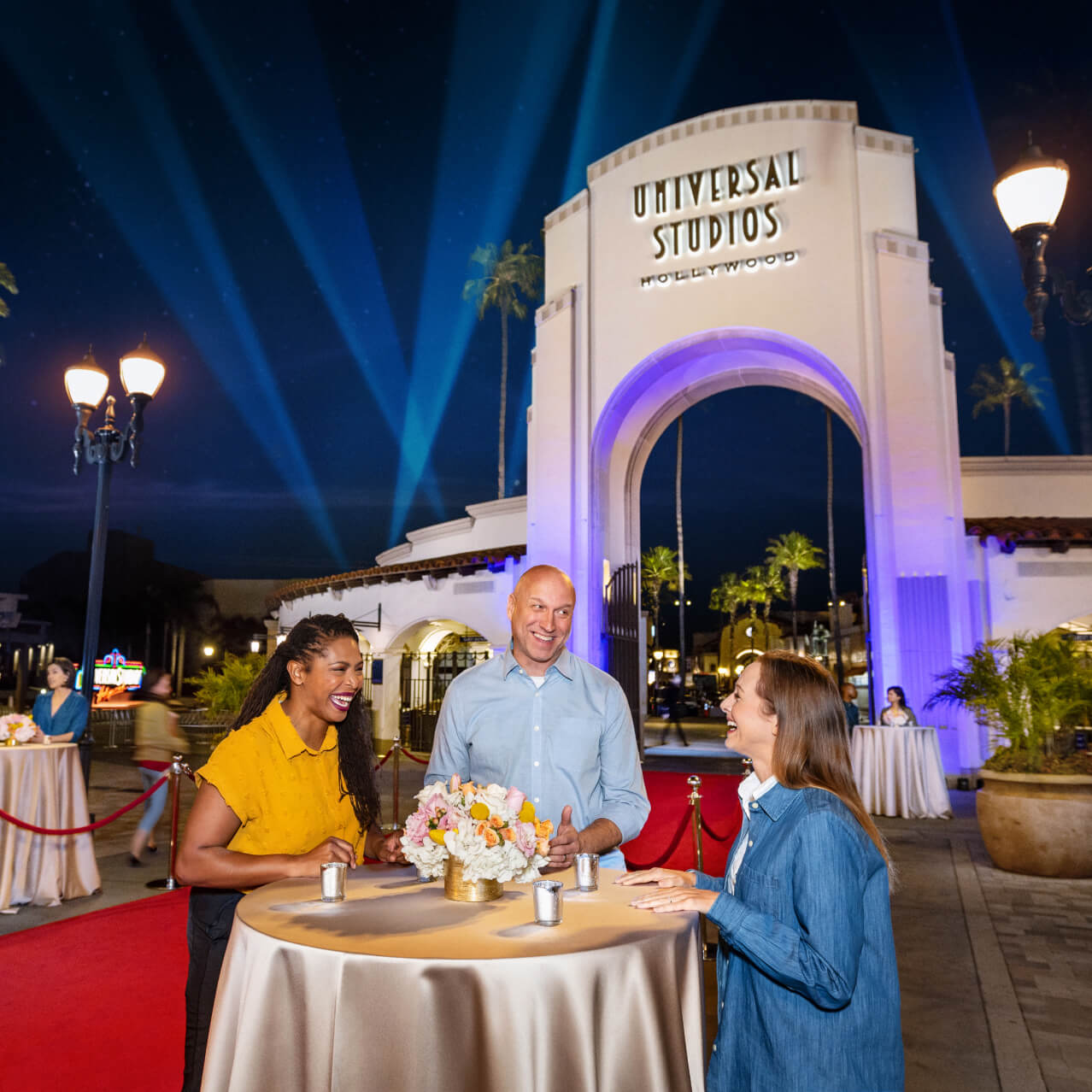 Guests enjoying a nighttime event at Universal Studios Hollywood’s entrance plaza with red carpet décor and illuminated archways.