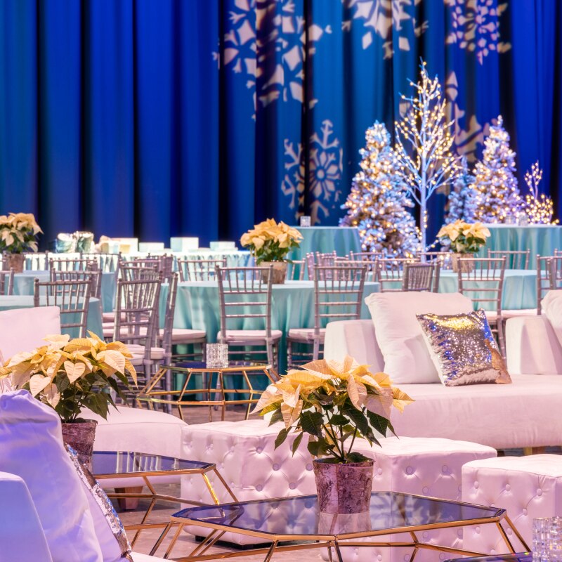 Tables covered in teal tablecloths and white floral arrangements with white holiday lights in the background.