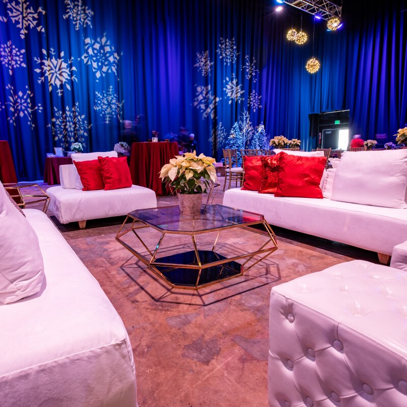 A venue full of white couches decorated with red pillows and white snowflakes projected onto the walls in the background.