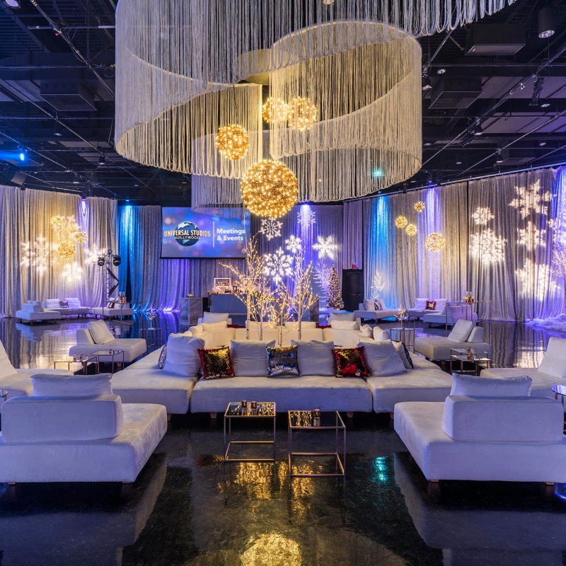 A venue full of white couches decorated with white holiday lights and snowflakes projected onto the walls.