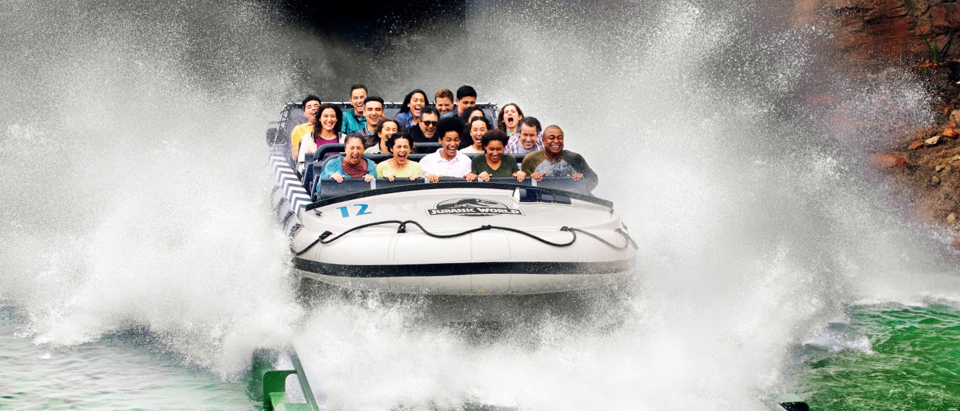 A boat full of guests cruising through the water as it makes a drop on Jurassic World – The Ride.