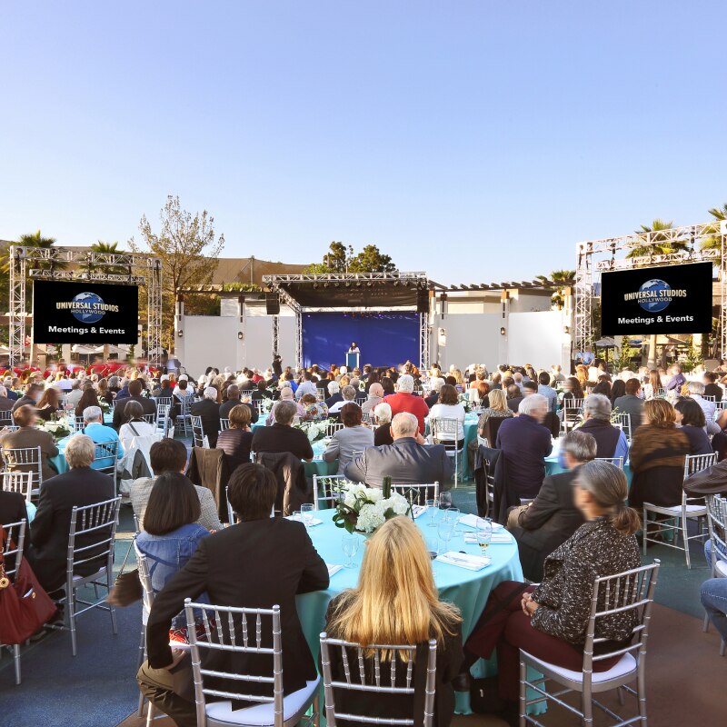 Dozens of tables with teal tablecloths and floral centerpieces set up for an event inside of Universal Plaza.