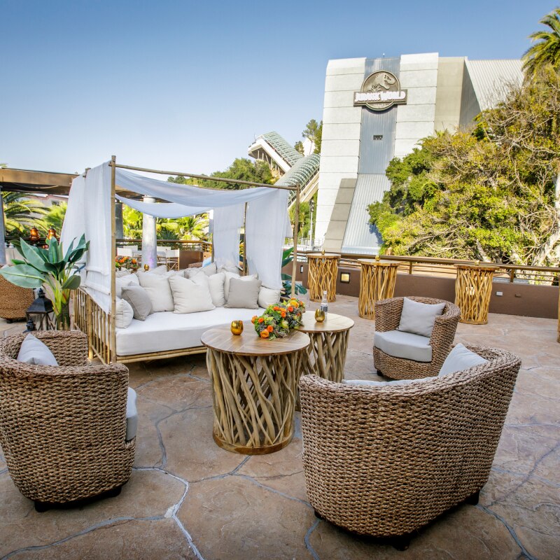 Straw seats and a bamboo daybed with tables set up for an event.