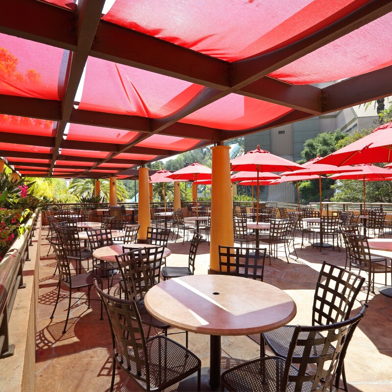 Dozens of round tables with chairs and red umbrellas.