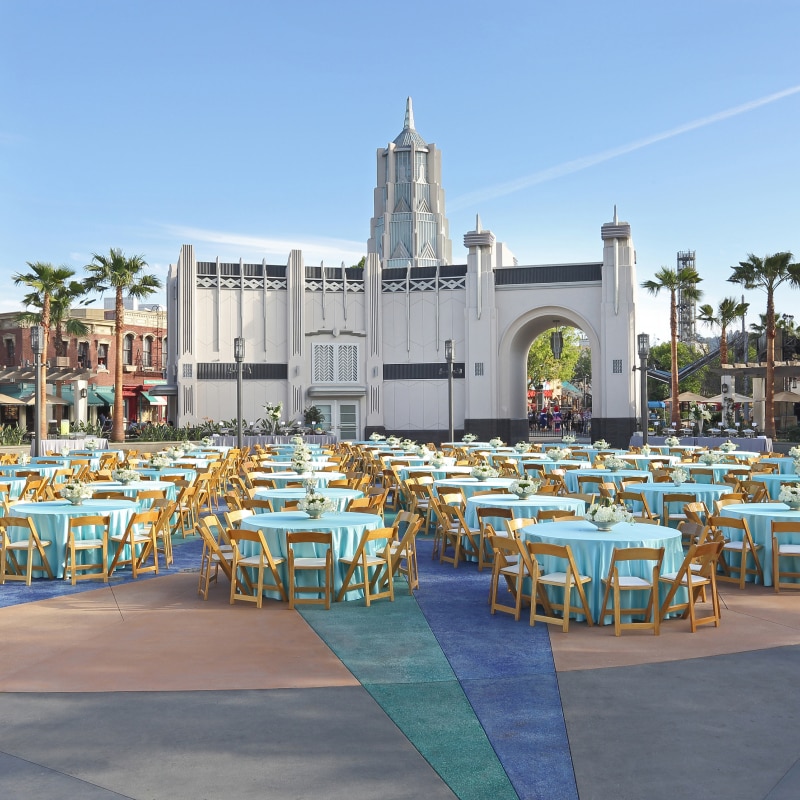 Dozens of tables with teal tablecloths and floral centerpieces set up for an event inside of Universal Plaza.
