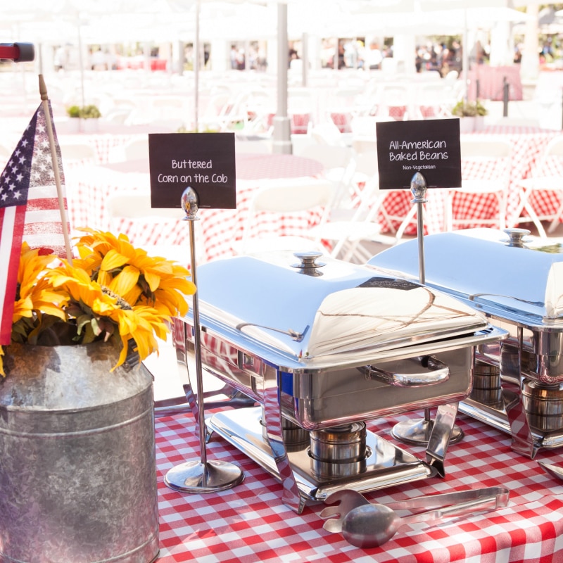 Silver buffet serving trays set up on a table with red checkered tablecloths for an event inside of Universal Plaza.