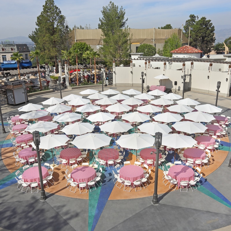 An aerial view of tables with red checkered tablecloths and white umbrellas set up for an event inside of Universal Plaza.