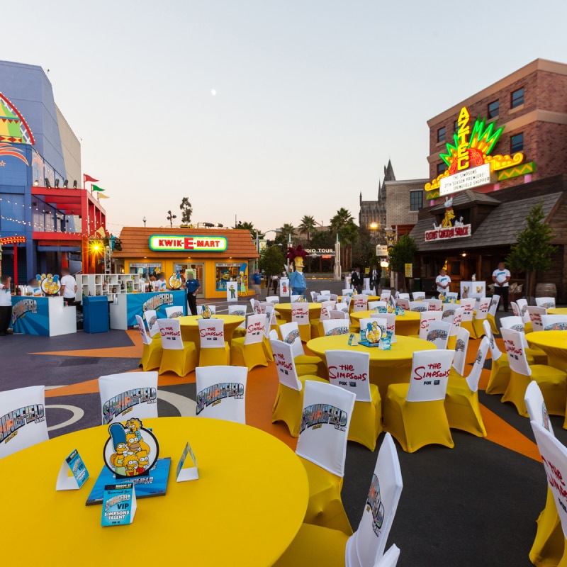 Dozens of tables decorated with The Simpsons themed decor in front of Krustyland.