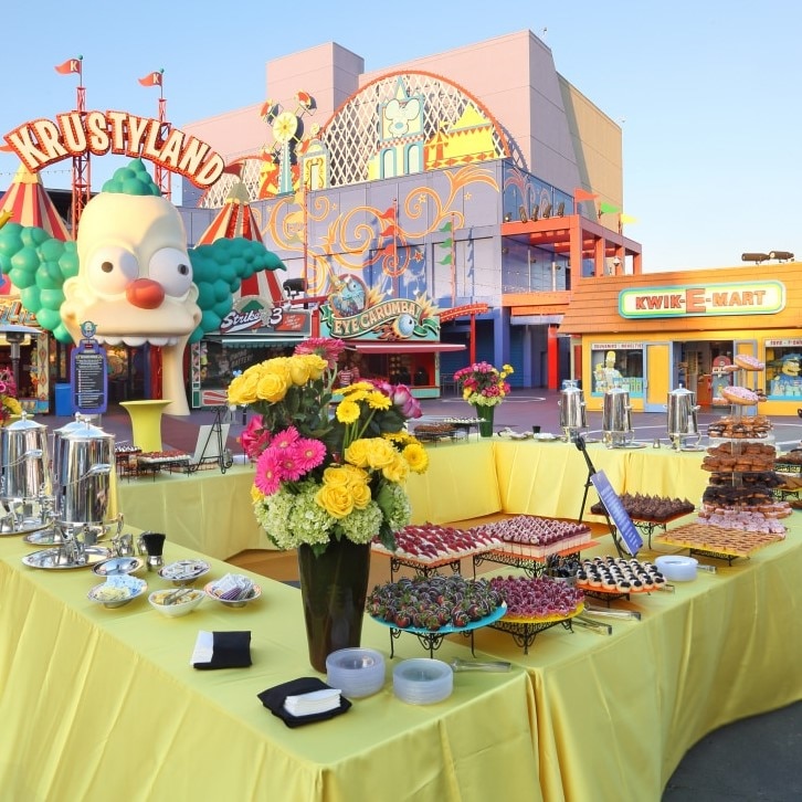 Tables topped with drinks and desserts for an event in front of Krustyland.