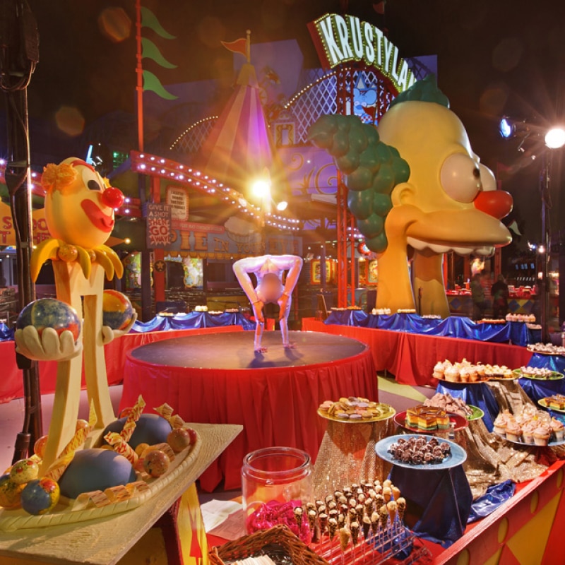 A buffet style spread including desserts and drinks set up in front of Krustyland.