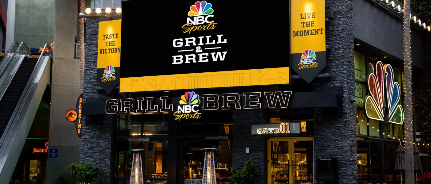 Exterior of NBC Sports Grill & Brew restaurant entrance with illuminated signage.