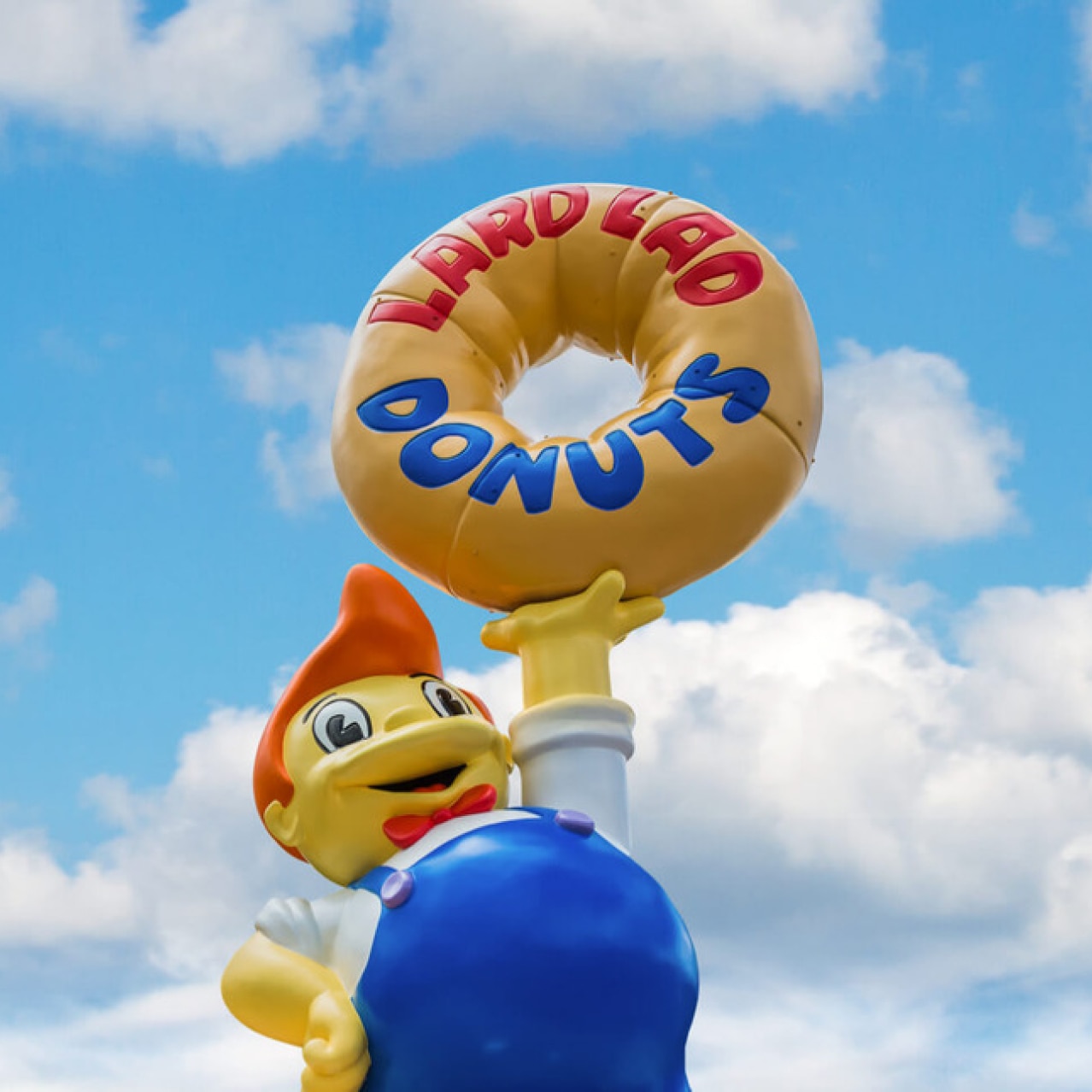 A large statue holding a donut with the words Lard Lad Donuts.