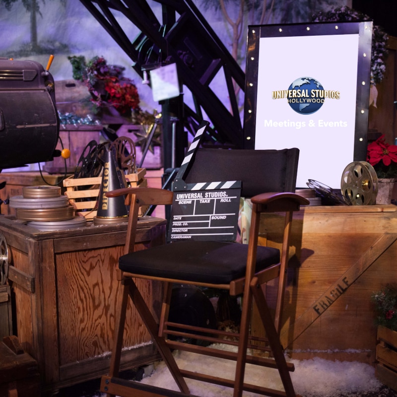 A director's chair with a clapperboard sitting on the seat in front of a sign with the Universal Studios Hollywood logo in the center.