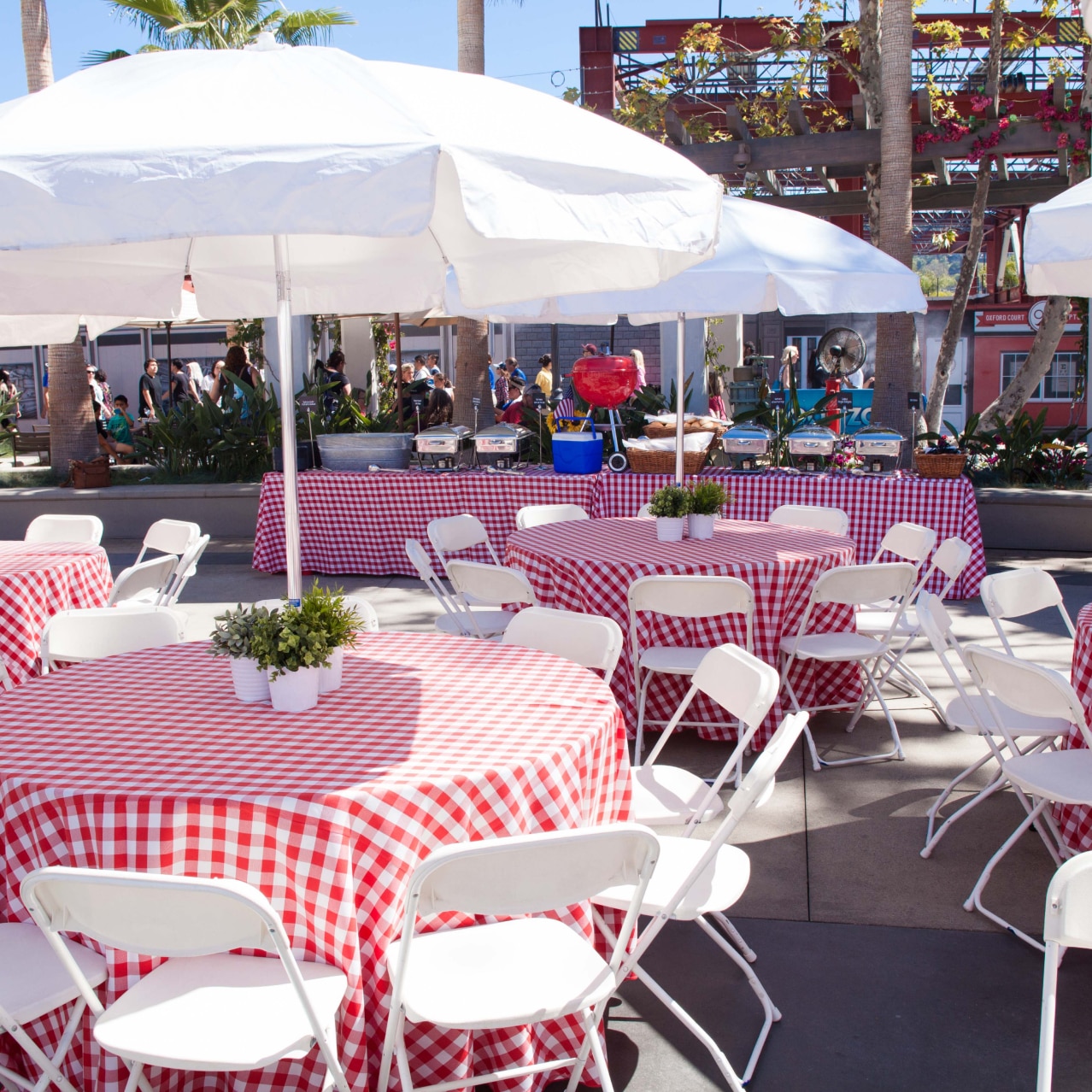 Tables with red checkered tablecloths and white umbrellas set up for an event inside of Universal Plaza.