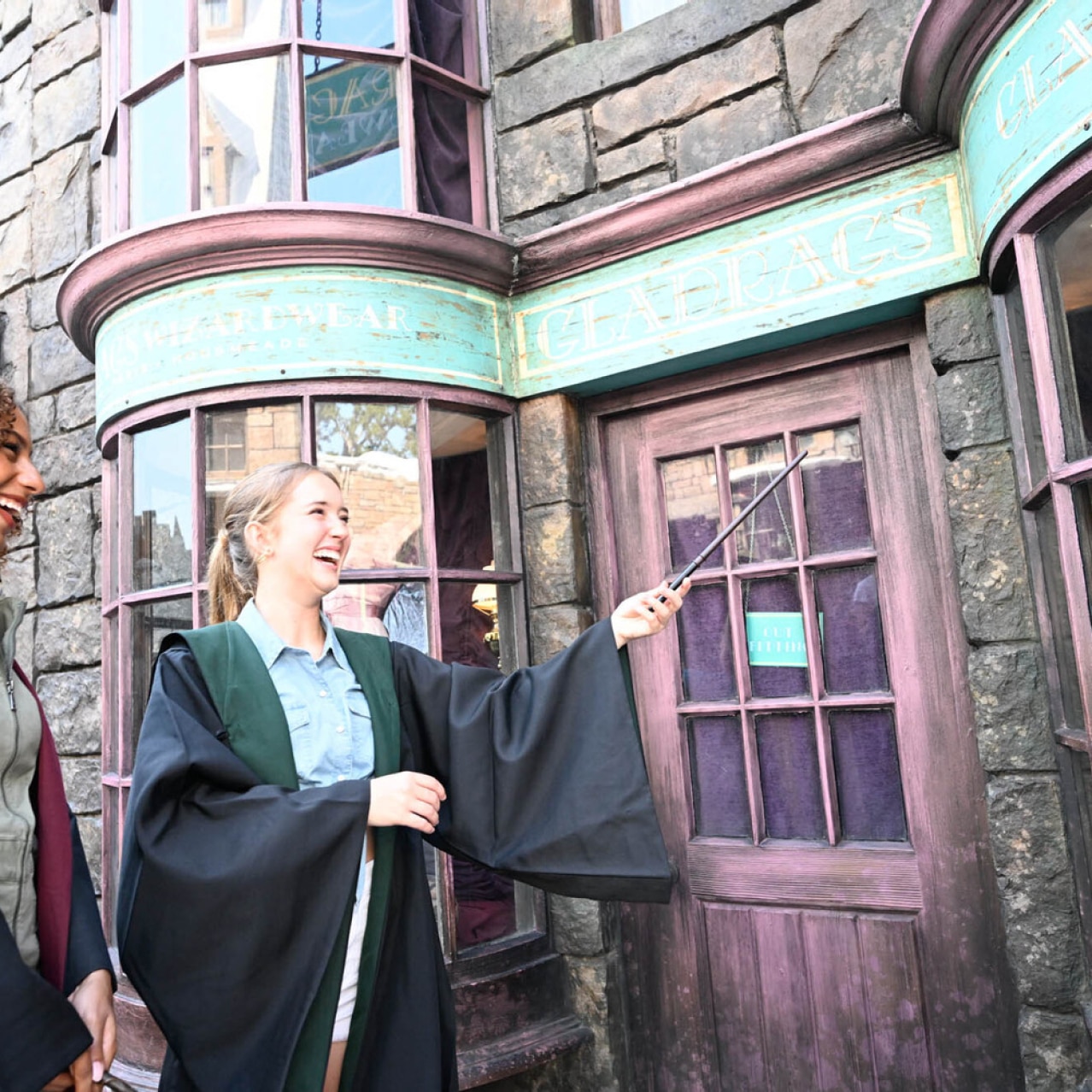 Two wizards standing in front of a storefront in Hogsmeade as one of them holds up their wand.
