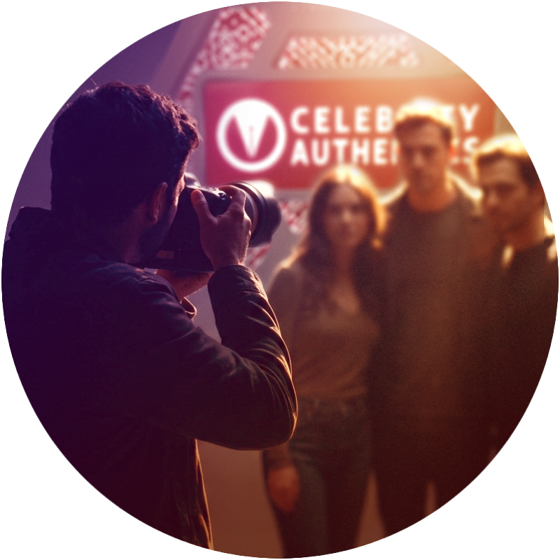 A group of friends posing in front of a “CELEBRITY AUTHENTICS” sign as a photographer in the foreground takes their picture.