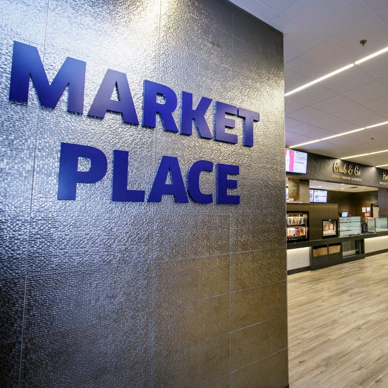 Large Marketplace wall sign leading to concession area with candy displays and counters labeled Grab & Go, Hot Food, and The Café.