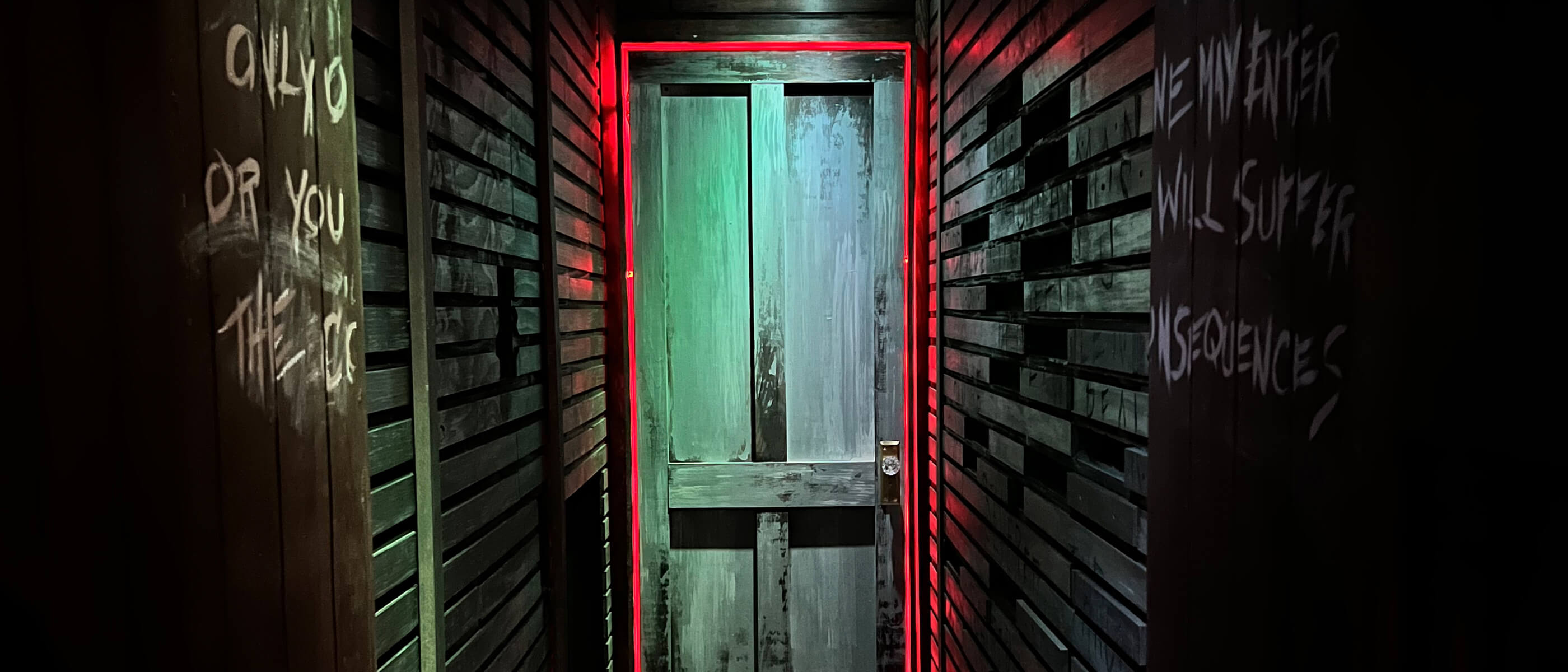A wooden door surrounded by a red light at the end of a hallway with white writing.