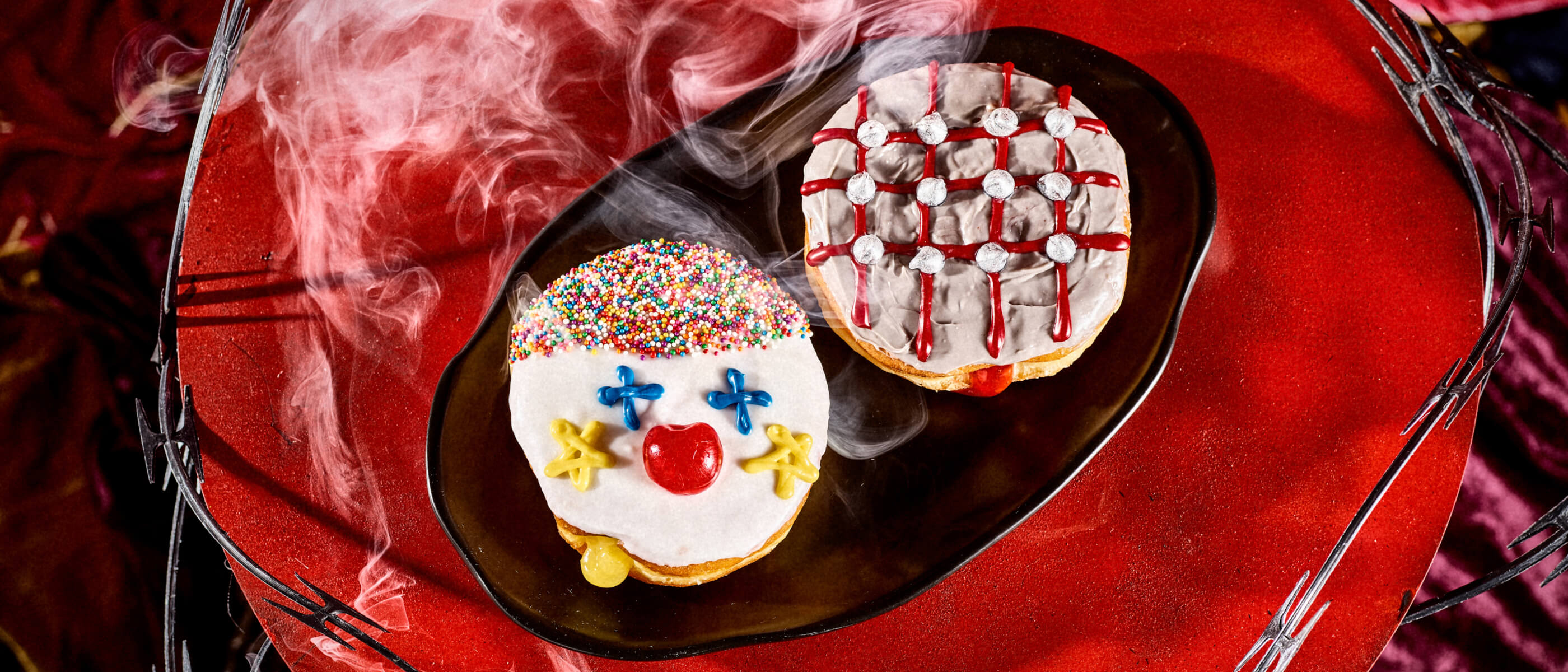 Voodoo Doughnut horror themed donuts—Creepy Clown and Hellraiser Pinhead—served on a dark barbed wire platter.
