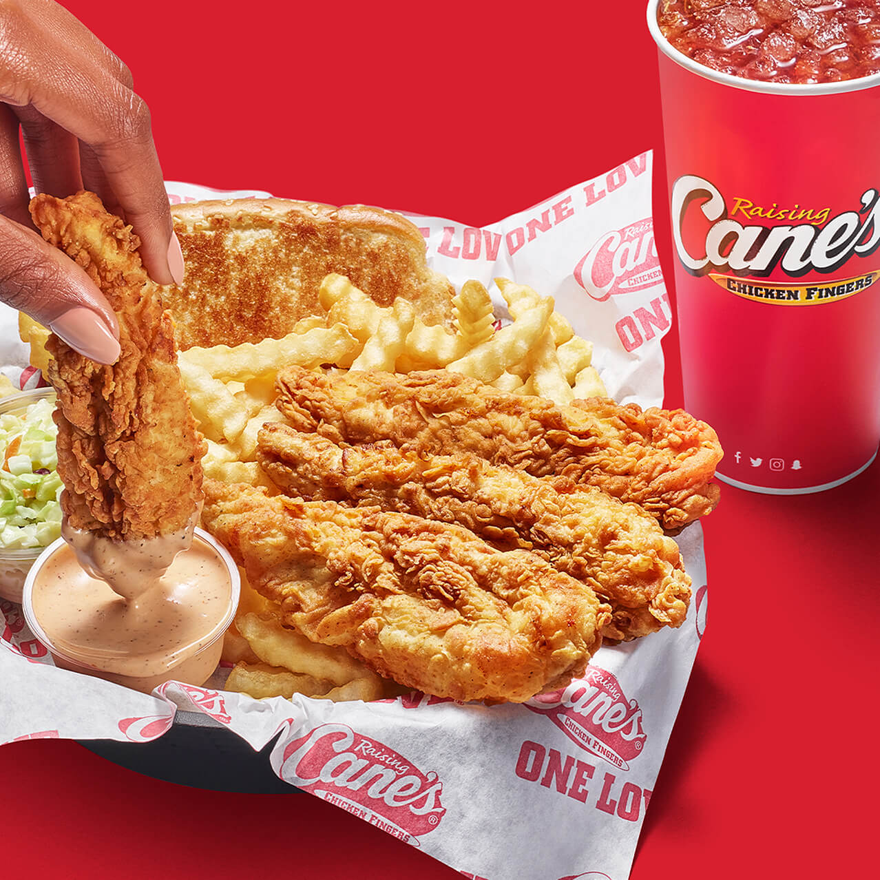 Hand dips a chicken finger in sauce inside a meal basket from Raising Cane’s Chicken Fingers at Universal CityWalk Hollywood.