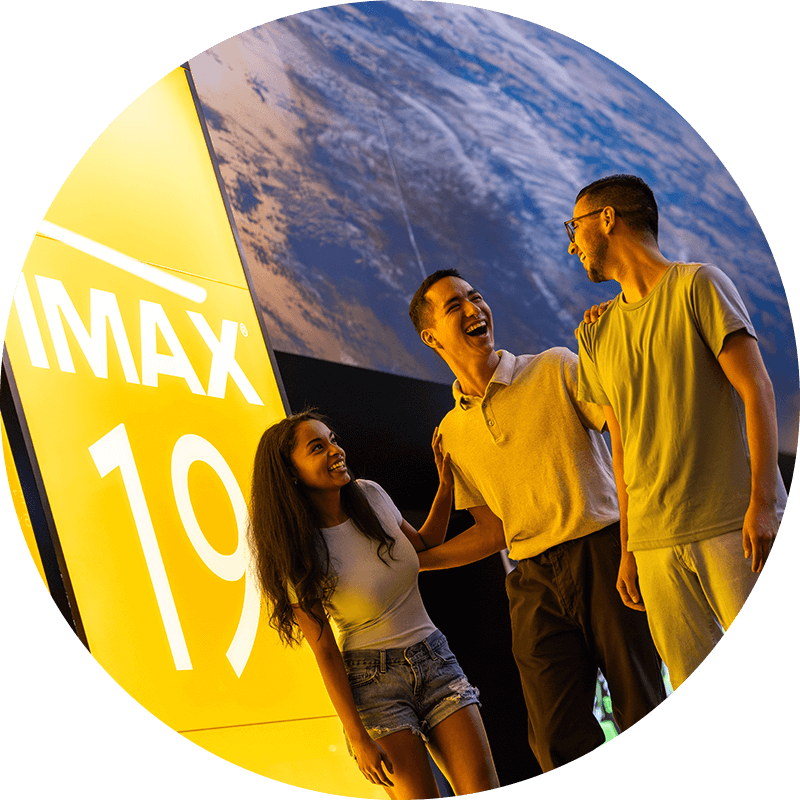 Three friends laugh in front of a sign that reads “IMAX 19” inside Universal Cinema at Universal CityWalk Hollywood.