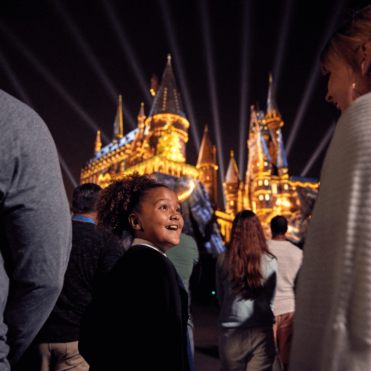 A little girl looks back at her mom while viewing the castle projection show, “The Magic of Christmas at Hogwarts™ Castle” during Holidays at Universal.