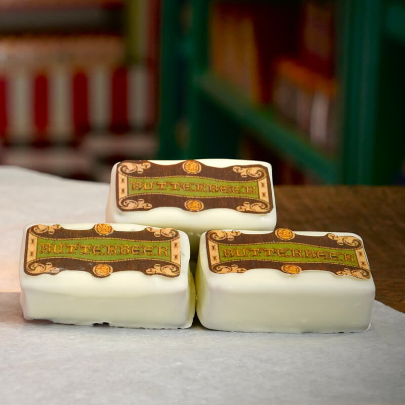 A plated puff pastry topped with decorative cream and a “BUTTERBEER” sign, on a wooden table with windows in the background.