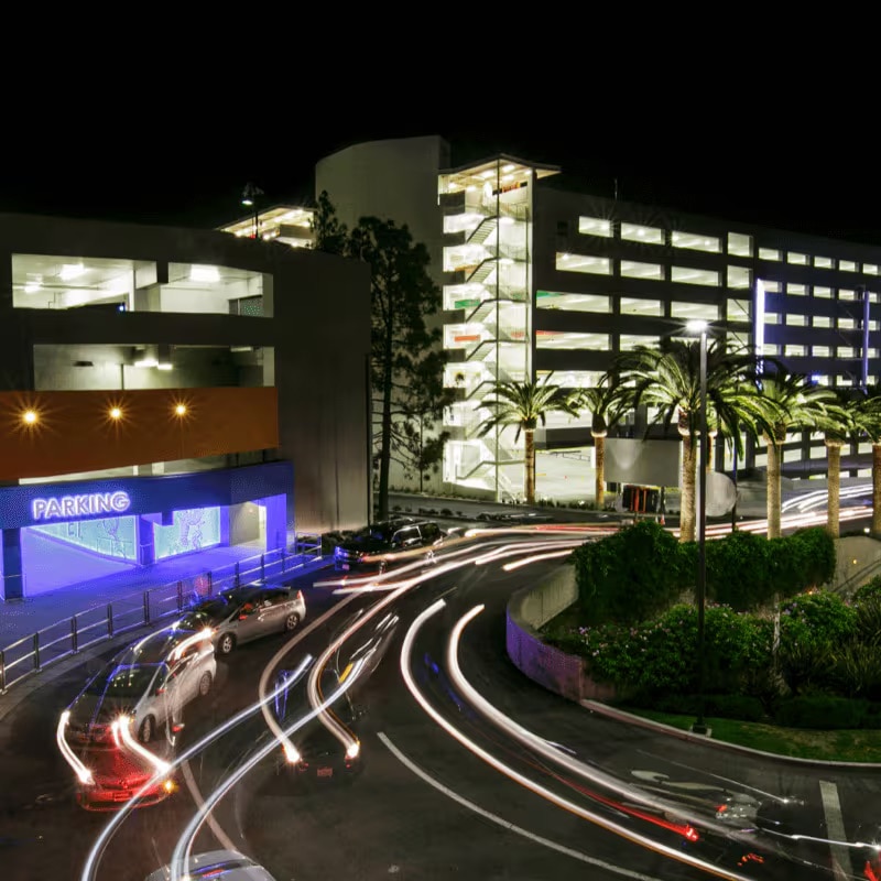 Exterior of parking garage lit up at night with cars entering and exiting.