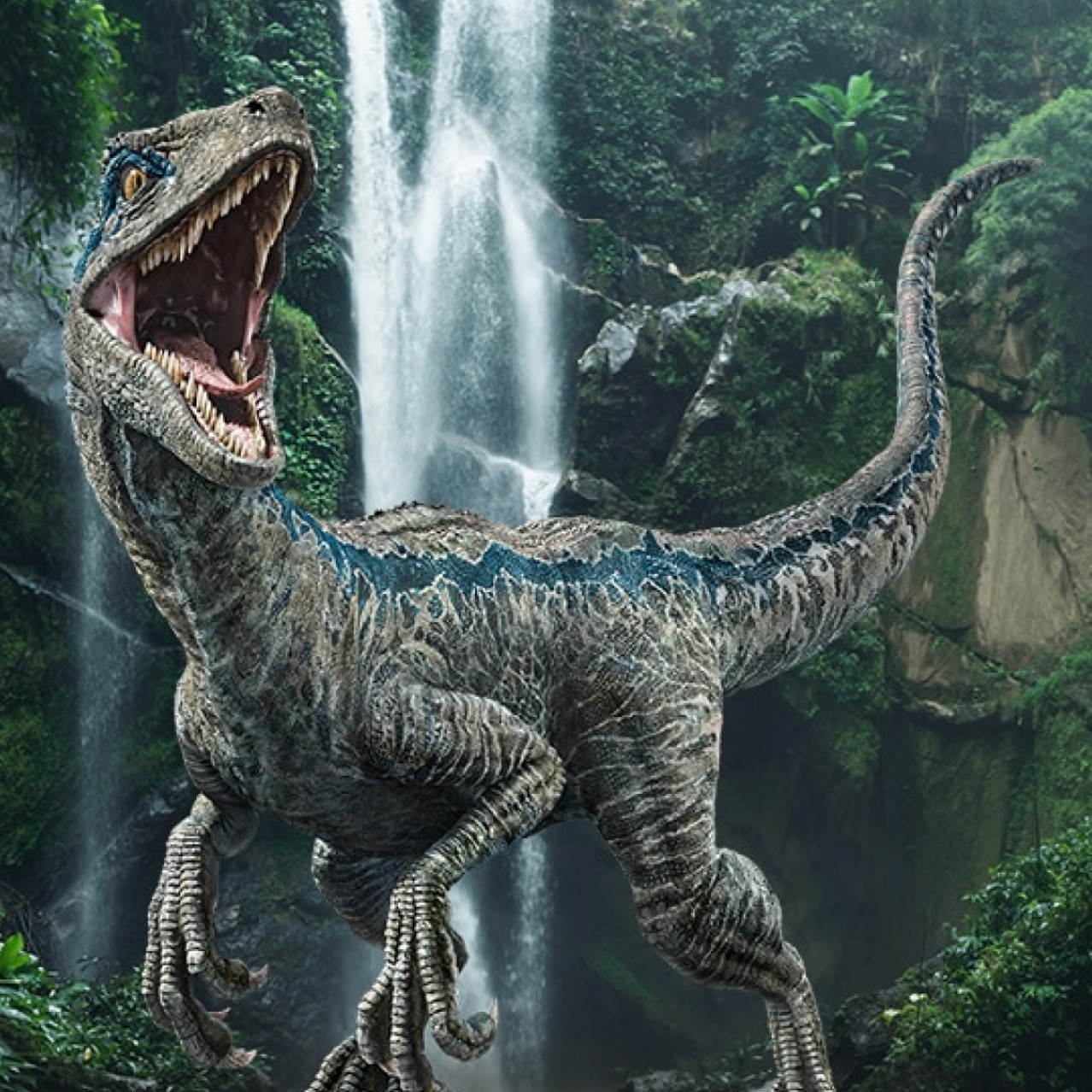 Blue the Velociraptor stands in front of a lush forest with a waterfall.