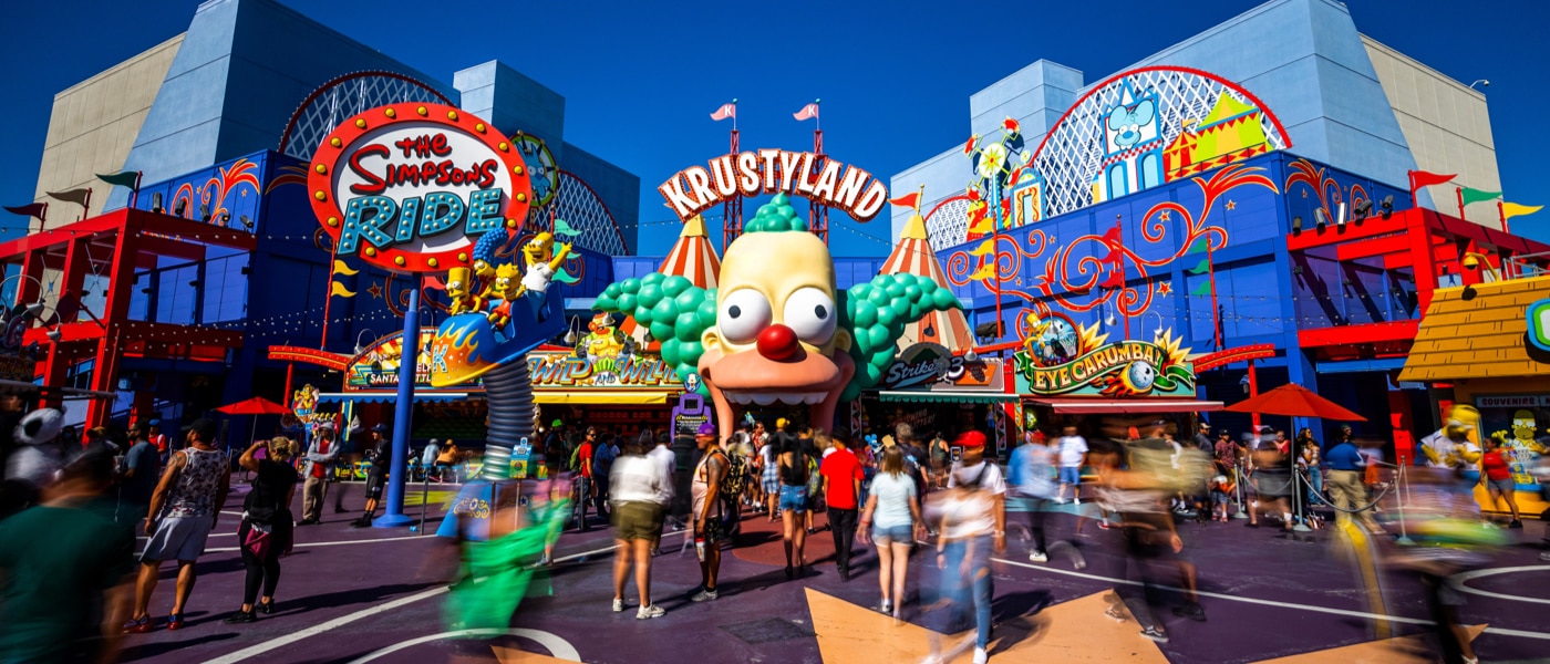 People walking around in front of The Simpsons Ride at Krustyland.