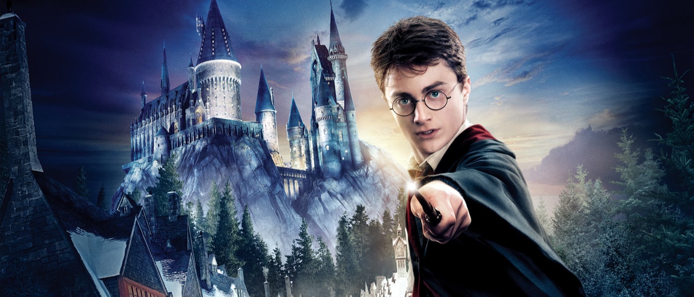 Harry Potter holding his wand in front of Hogwarts castle