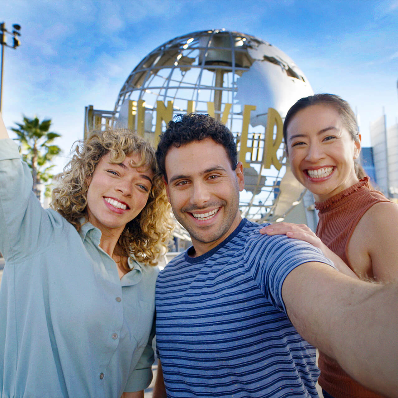 A group of friends smile for a selfie in front of the globe at the entrance to Universal Studios Hollywood.