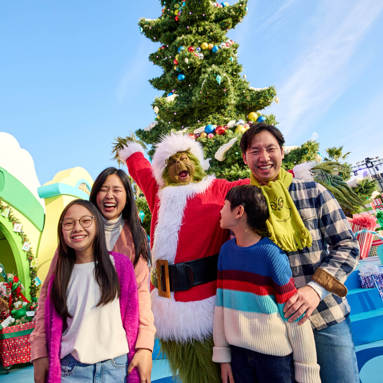 A family of four posing with the Grinch in front of a Christmas tree in Whoville.