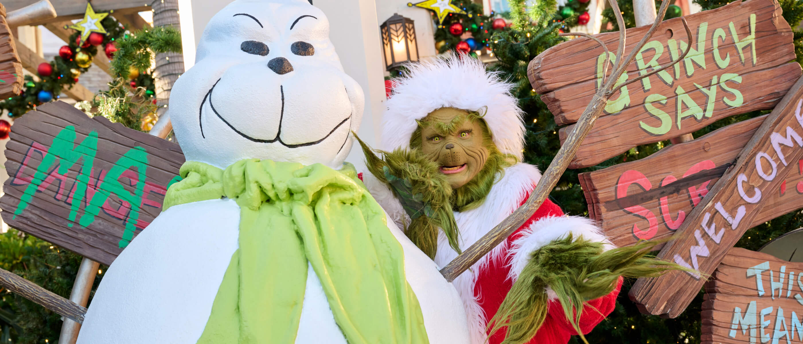 The Grinch, in his Santa hat and coat, posing mischievously with a green-scarved snowman that looks a lot like him.