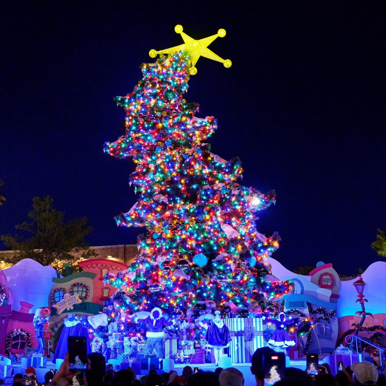 A stage featuring Who-ville landmarks and a towering, tilted, twinkle-lit Christmas tree with a yellow star topper.
