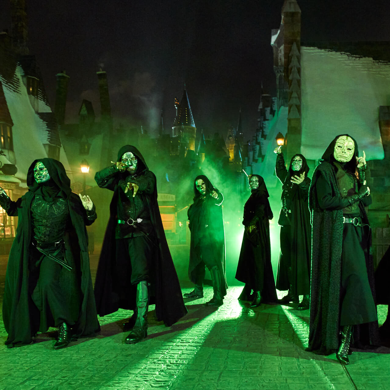 A group of figures in black hooded cloaks and metallic masks brandishing wands with Hogsmeade™ and Hogwarts™ castle visible behind them.