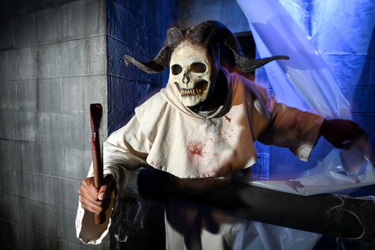 A skeletal scareactor with twisting black horns holds a bloody, wooden implement.