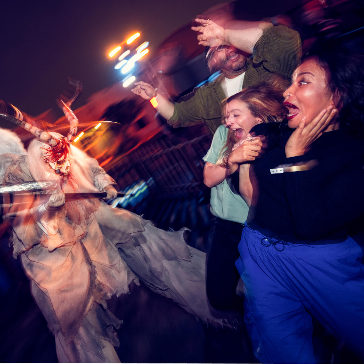 A skeletal scareactor with bloody horns holds a scythe and lunges towards three screaming guests.