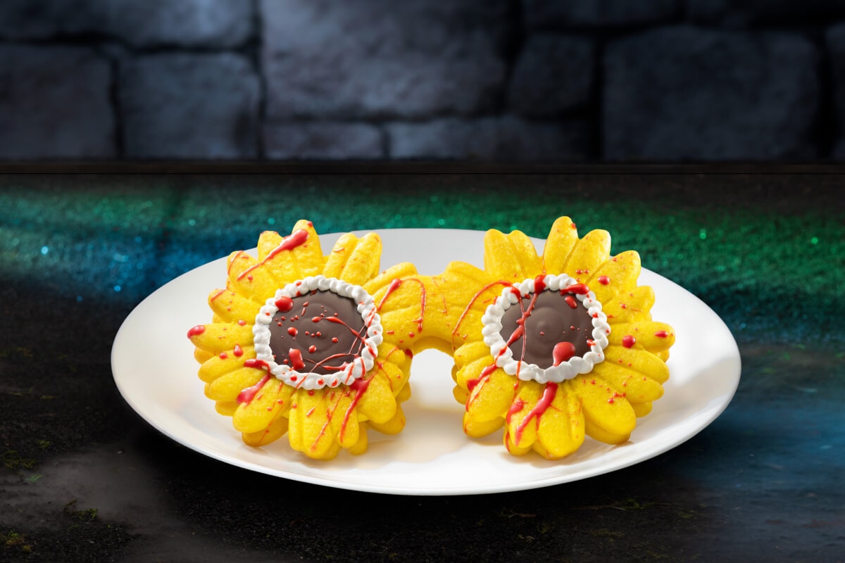 A plate with red-drizzled dessert of yellow flowered sunglasses with chocolate lenses against a green carpet and stone wall.