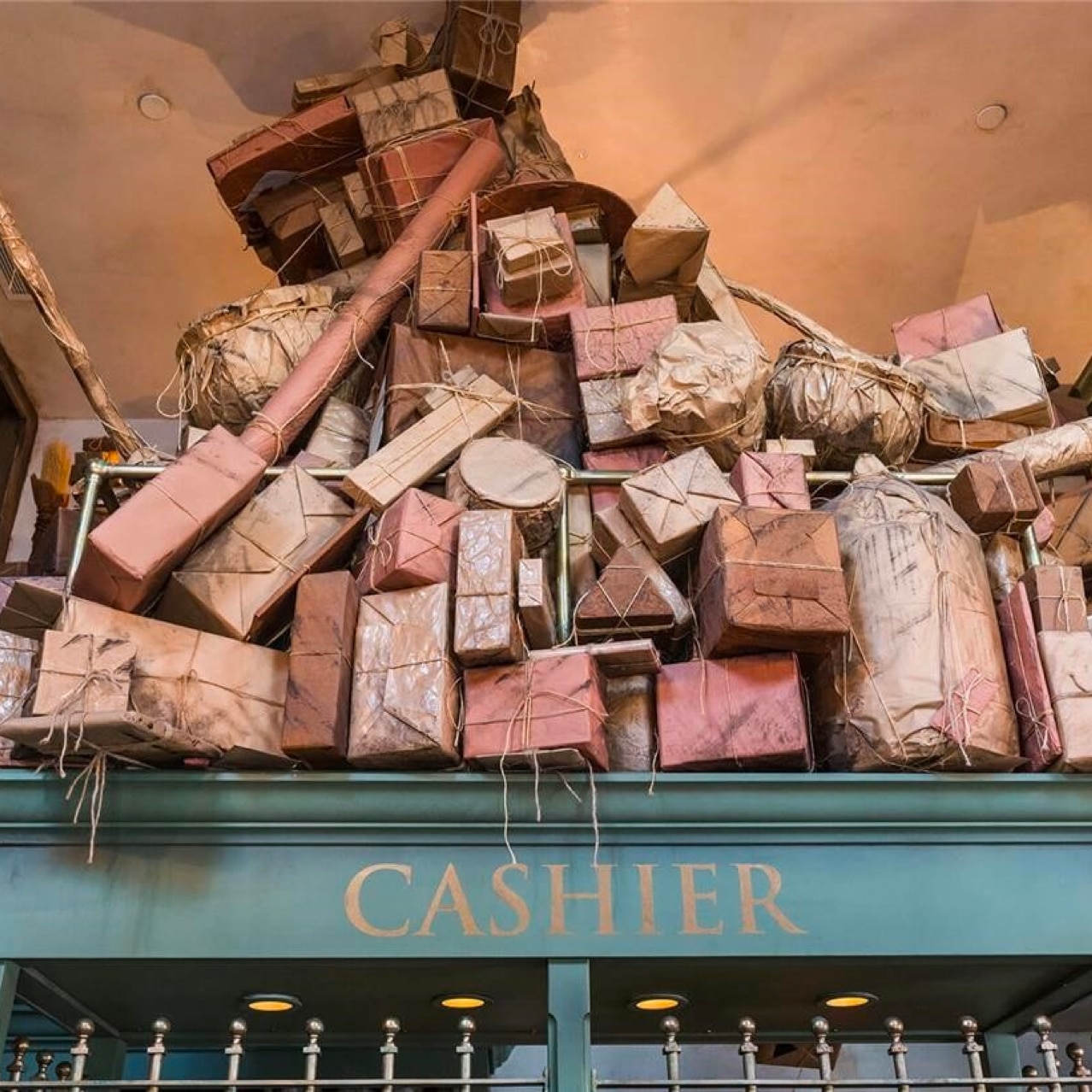Multiple wrapped objects on top of a green shelf with the word "Cashier" on it and shelves surrounding it.